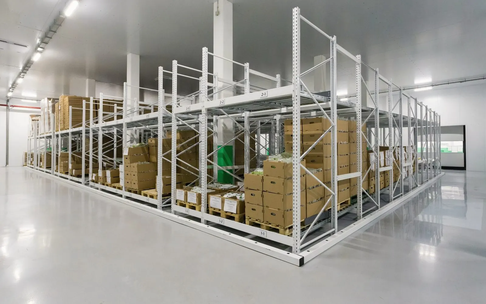 White steel racking with boxed stock on pallets in a bright warehouse.